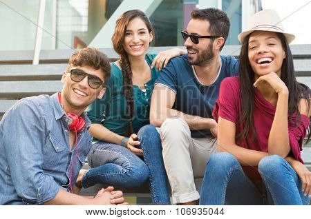 Closeup shot of young friends sitting on staircase having fun. Happy girls and guys smiling and looking at camera. Young men and young women stay together.