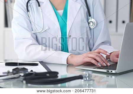 Close-up of female doctor hands typing on laptop computer. Physician at work. Medicine, healthcare and help concept.