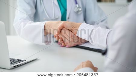 Doctor and patient shaking hands, close-up.  Physician talking about medical examination results. Medicine, healthcare and trust concept.