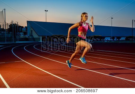 Runner sprinting towards success on run path running athletic track. Goal achievement concept. Female athlete sprinter doing a fast sprint for competition on red lane at an outdoor field stadium.