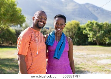 Portrait of black sporty couple looking at camera at park with copy space. Happy mature man and smiling woman relaxing after jogging in the park. African american man and woman resting after exercise.