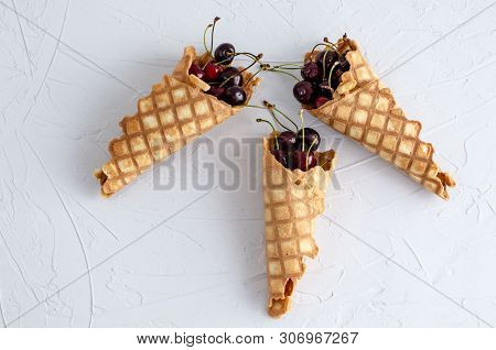 Ice Cream Cone Filled With Cherries On A Light White Concrete Background.