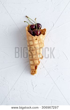 Ice Cream Cone Filled With Cherries On A Light White Concrete Background.