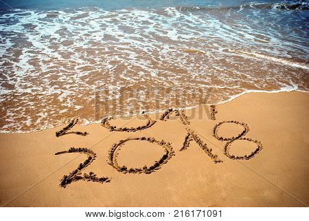 New Year 2018 is coming concept - inscription 2017 and 2018 on a beach sand the wave is covering digits 2017. New Year 2018 celebration on New Year`s Eve tropical island travel tour.