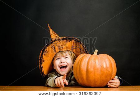 Child With Pumpkin Pointing To You. Preparation Halloween Holiday. Cute Boy In Witch Hat With Hallow