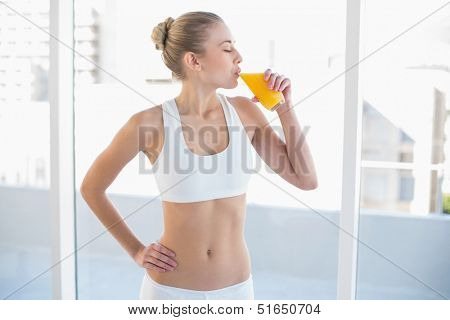 Peaceful young blonde model in white sportswear enjoying orange juice