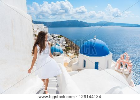 Santorini travel tourist woman on vacation in Oia walking on stairs. Person in white dress visiting the famous white village with the mediterranean sea and blue domes. Europe summer destination