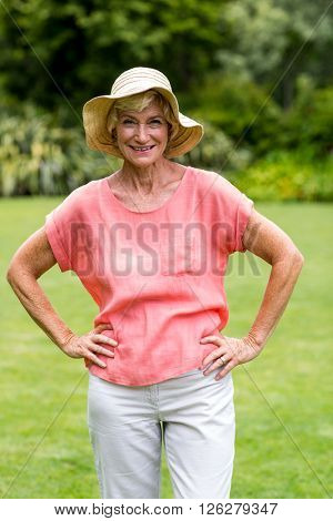 Portrait of happy senior woman with ahnd on hip at yard