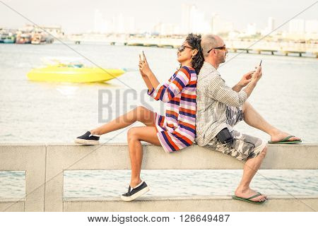 Travelers couple in disinterest moment with mobile phones at Pattaya beach - Apathy and addiction concept with bored people using smartphones - Soft desaturated filter with slight tilted horizon