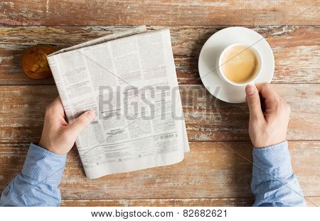 business, information, people and mass media concept - close up of male hands with newspaper, muffin and coffee cup on table