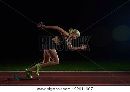 woman  sprinter leaving starting blocks on the athletic  track. Side view. exploding start