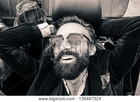 Fashion portrait of young bearded man ready for road trip - Cheerful hipster guy sitting in car lokking the sky - Black and white editing - Soft focus on beard - Warm vintage retro filter