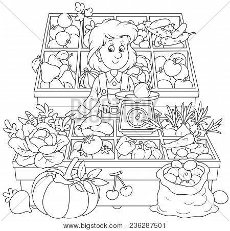 Greengrocer In A Market. Smiling Girl Trader Standing Behind Her Counter Surrounded By Vegetables An