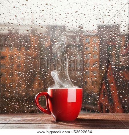 Steaming coffee cup on a rainy day window background