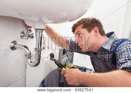 Young Plumber Fixing A Sink In Bathroom