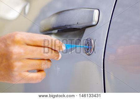 Closeup hands of locksmith using pick tools to open locked car door.