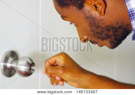 Closeup head and hands of locksmith using pick tools to open locked door.