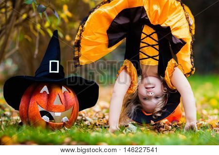 Little girl in witch costume playing in autumn park. Child having fun at Halloween trick or treat. Kids trick or treating. Toddler kid with jack-o-lantern. Children with candy bucket in fall forest.