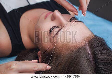 Master corrects makeup gives shape and thread plucks eyebrows in a beauty salon. Professional care for face and eyebrows.