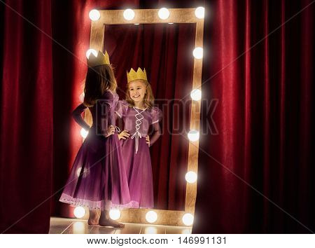 Cute little actress. Child girl in Princess costume on the background of theatrical scenes and mirrors.