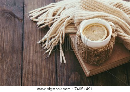 Cup of hot tea with lemon dressed in knitted warm winter scarf on brown wooden tabletop, top view point