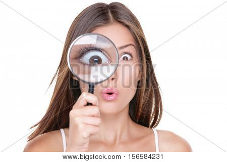 Funny expression. Shocked woman looking through a magnifying glass. Surprised Asian girl looking astonished discovering clues with big eyes through a magnifying glass, isolated on white background.