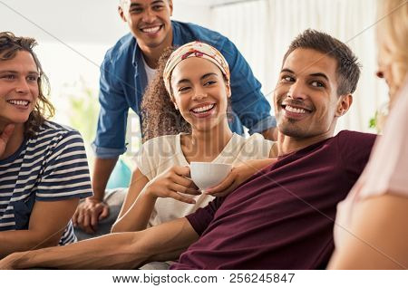 Young friends meeting and enjoying coffee after a long time. Group of happy multiethnic men and women in conversation while drinking tea. Guys and smiling girls talking and discussing at home.