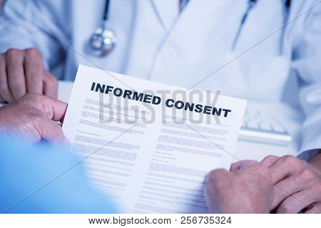 closeup of a senior caucasian man, at the doctors office, reading an informed consent document in front of a caucasian doctor man, in a white coat, sitting both at the doctors desk