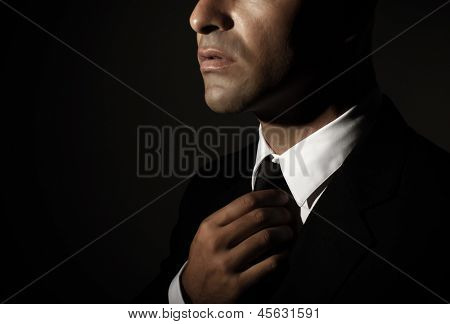 Young handsome man fixed tie isolated on black background, face part, successful businessman, mens fashion, glamour concept