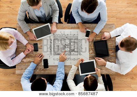 business, people, architecture and team work concept - close up of architects team with blueprint, smartphones and tablet pc computers sitting at table in office