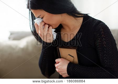 burial, people, grief and mourning concept - close up of unhappy crying woman with photo frame and paper wipe at funeral day