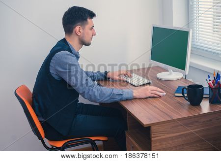 Young man office worker sitting at his desk working at computer with Chromakey on monitor. Office concept with working environment