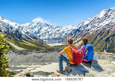 Backpackers couple hiking looking at Mt Cook view on mountains tramping in New Zealand. People hikers relaxing during hike in alps of south island.