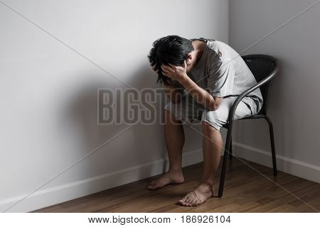 Depressed sad poor young man sitting on chair in corner of empty room, sadness and depression concept