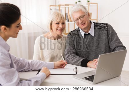 Older Couple Considering New Home Purchase Talking With Real Estate Agent And Looking At Laptop