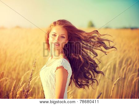 Beauty Girl Outdoors enjoying nature. Beautiful Teenage Model girl with long healthy blowing hair running on the Spring Field, Sun Light. Glow Sun. Free Happy Woman. Toned in warm colors