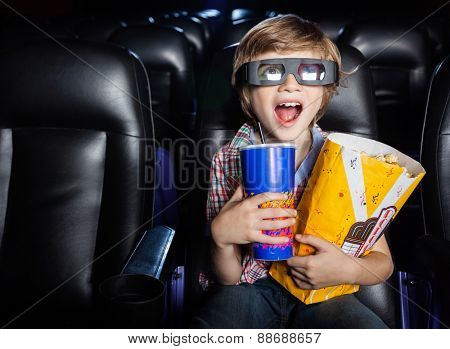 Surprised boy holding snacks while watching 3D movie in cinema theater