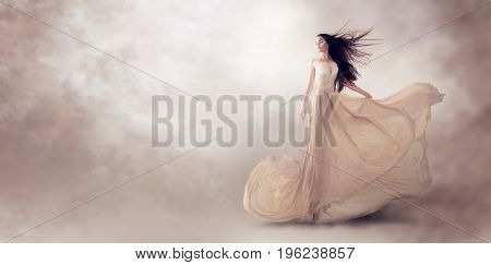 Fashion model in beautiful luxury beige flowing chiffon dress, Woman in long flying evening dress with a gown, Stunning fantasy model. Silk fabric waving on wind. Satin Cloth Flowing, Waves of a dress