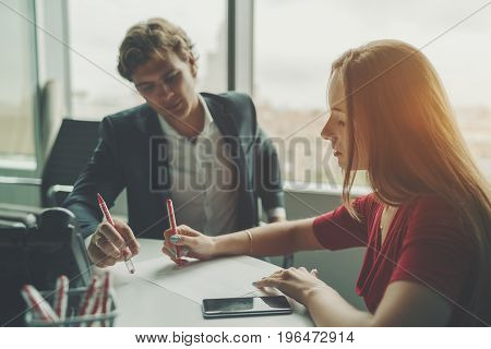 Attractive man entrepreneur having work conversation with his female beautiful co-worker businesswoman explaining her colleague new development strategy using sheet of paper and pen during meeting