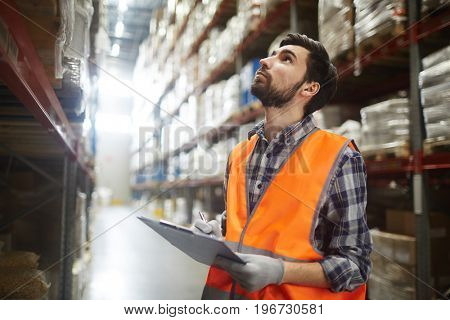 Portrait of warehouse worker looking up the tall shelves doing inventory control