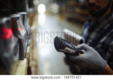 Side view closeup of bar code scanner in hand of unrecognizable warehouse worker doing inventory of stock