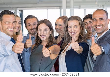 Group of happy business people showing sign of success. Successful business team showing thumbs up sign and looking at camera. Smiling businessmen and businesswomen cheering at office.