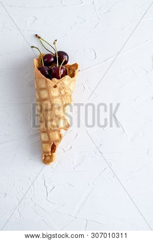 Ice Cream Cone Filled With Cherries On A Light White Concrete Background.