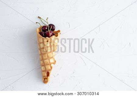 Ice Cream Cone Filled With Cherries On A Light White Concrete Background.