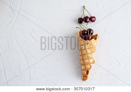 Ice Cream Cone Filled With Cherries On A Light White Concrete Background.