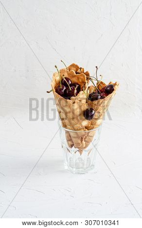 Three Ice Cream Cones Filled With Cherries In A Glass Beaker On A Light White Concrete Background.