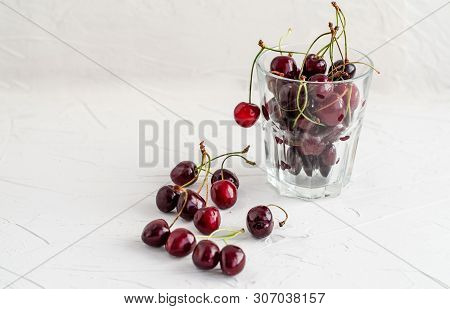 Ripe Fresh Red Sweet Cherry In A Glass Beaker On A White Concrete Background