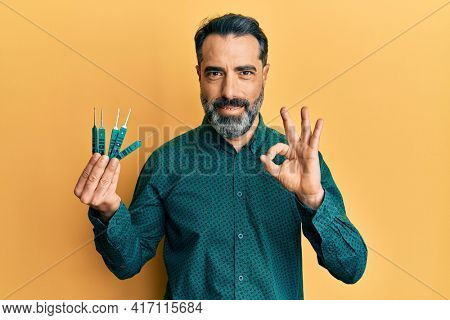 Middle age man with beard and grey hair holding picklock to unlock security door doing ok sign with fingers, smiling friendly gesturing excellent symbol 