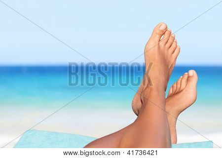 Vacation holidays. Woman feet closeup of girl relaxing on beach on sunbed enjoying sun on sunny summer day.