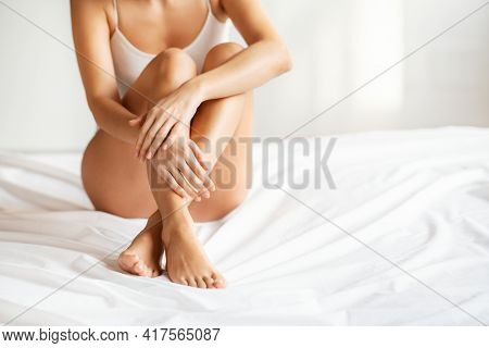 Detail of beautiful young woman hands and legs with perfect smooth soft skin after beauty treatment sitting on bed with copy space. Laser epilation, cosmetology, spa, and hair removal concept.